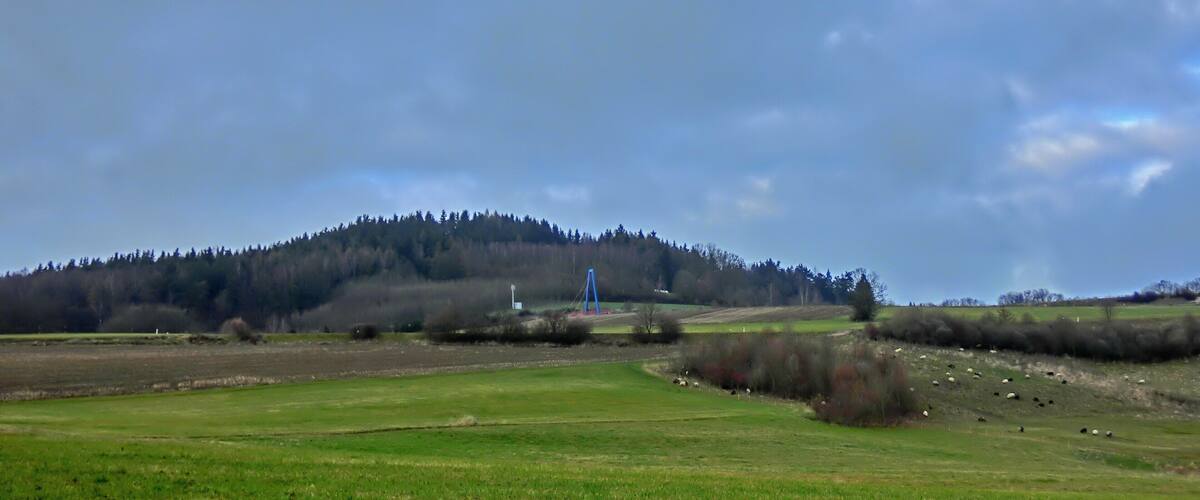 A rural landscape with a hill, grazing sheep, and a blue structure on the hill.