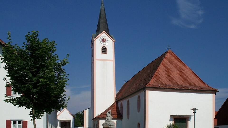 A church with a tall steeple and a clock, surrounded by a small village.