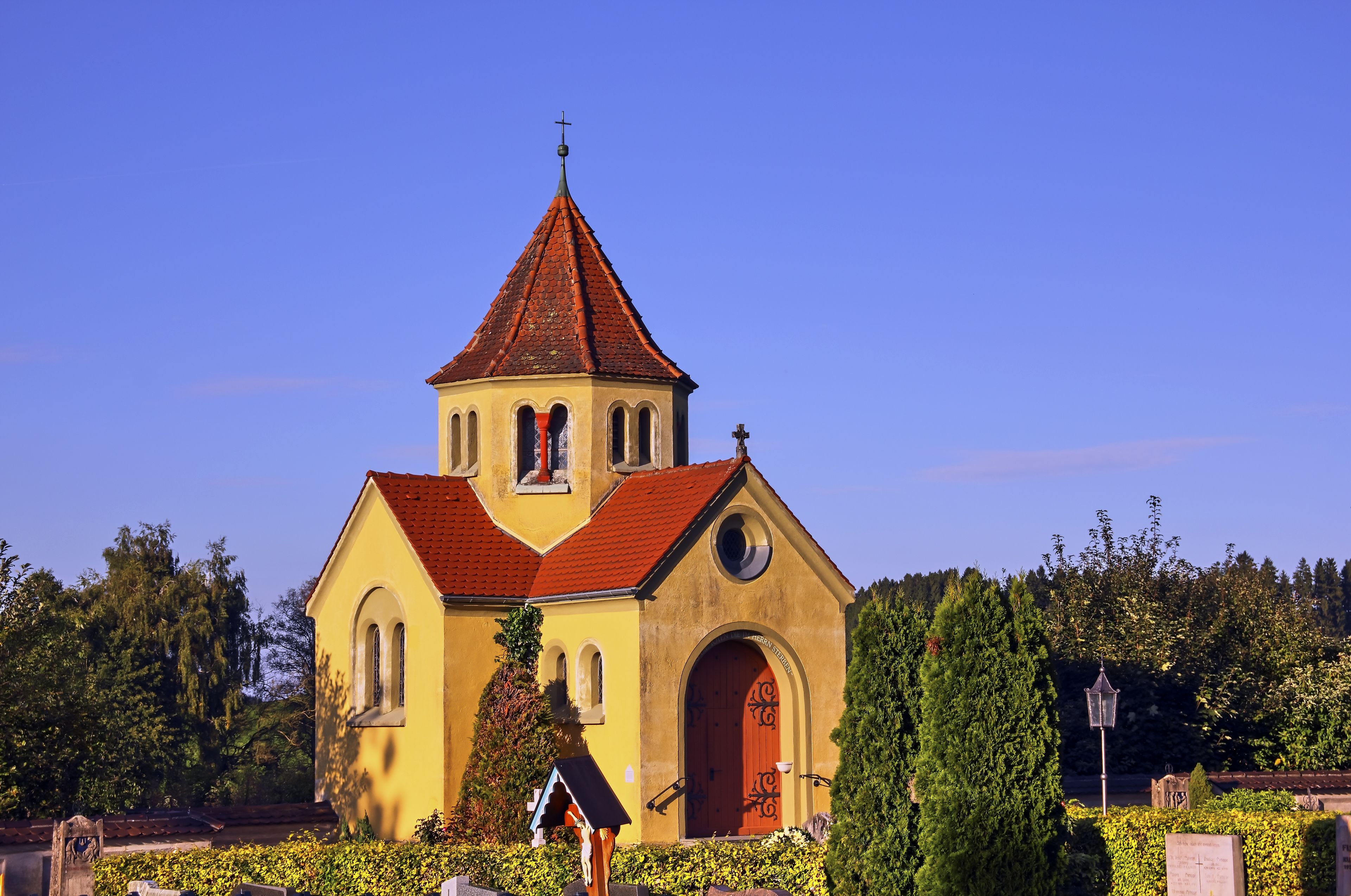 En kyrka med ett rött tegeltak och en gul fasad, omgiven av grönska.