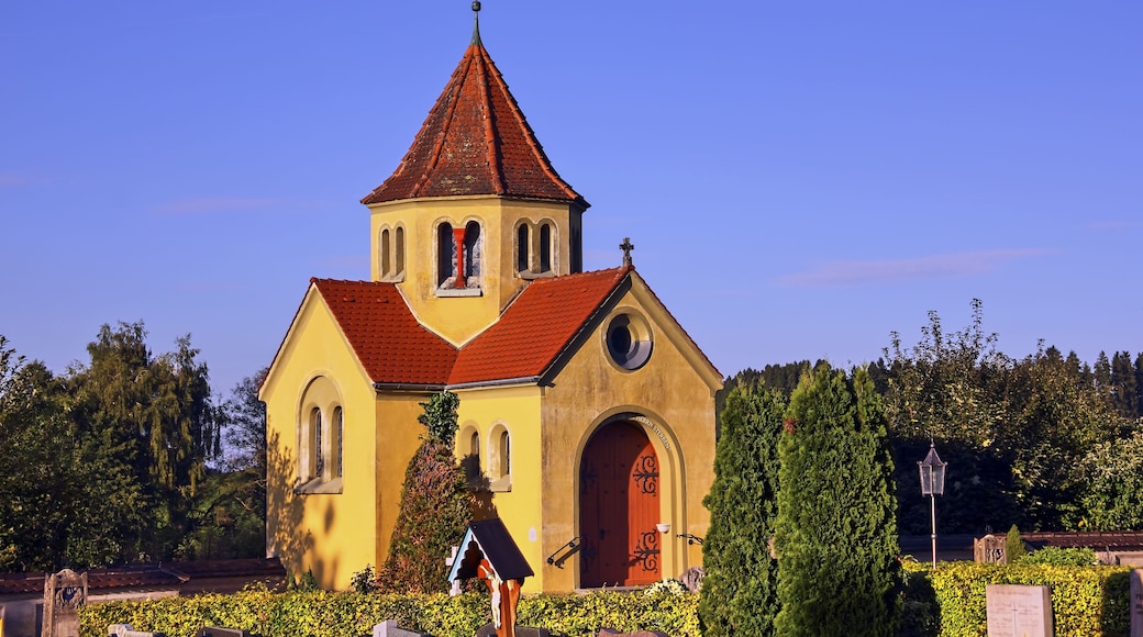 En kyrka med ett rött tegeltak och en gul fasad, omgiven av grönska.