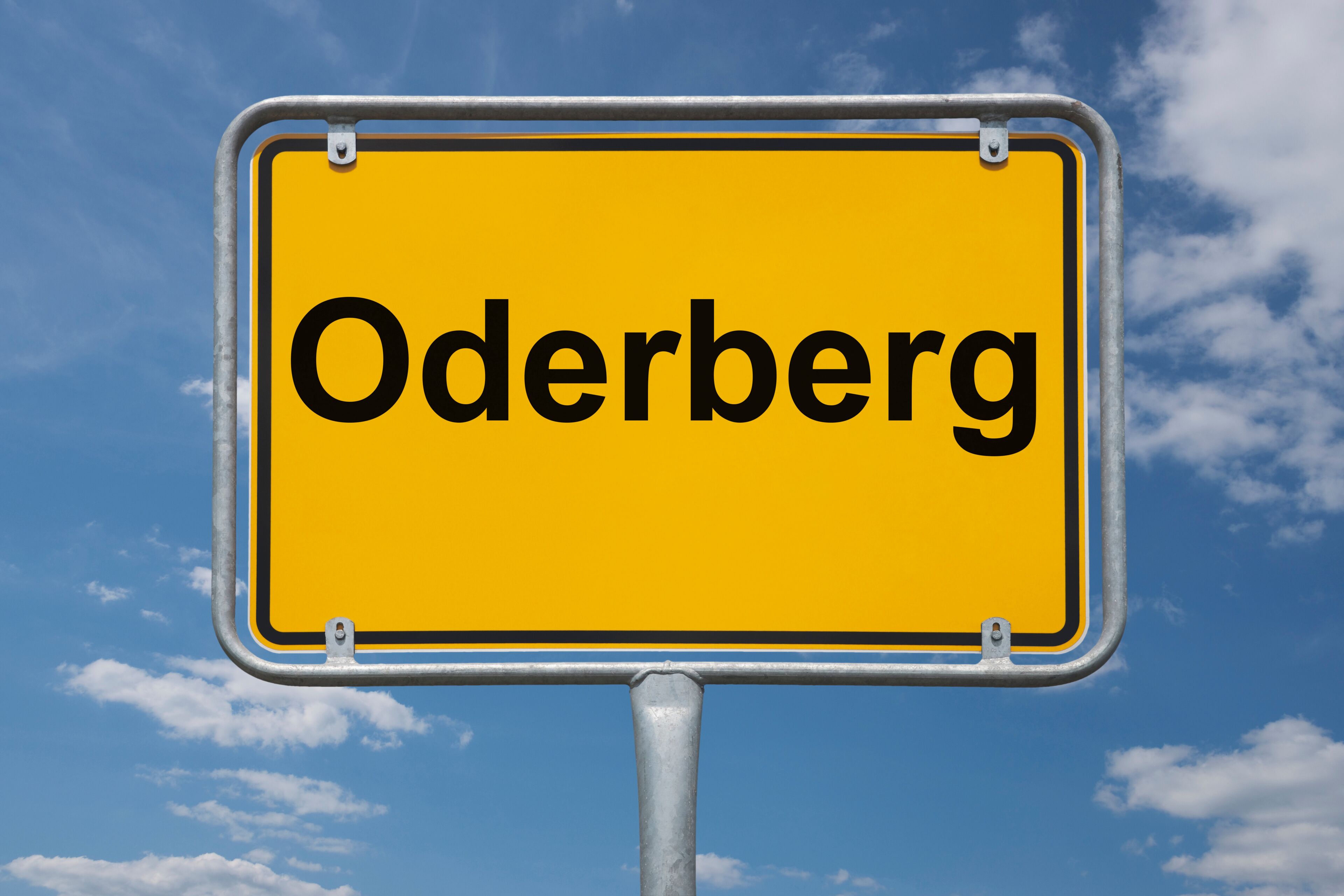 A yellow sign with the word "Oderberg" against a blue sky with clouds.