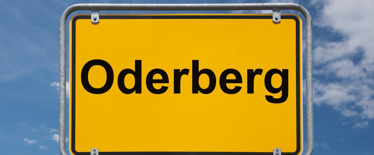A yellow sign with the word "Oderberg" against a blue sky with clouds.