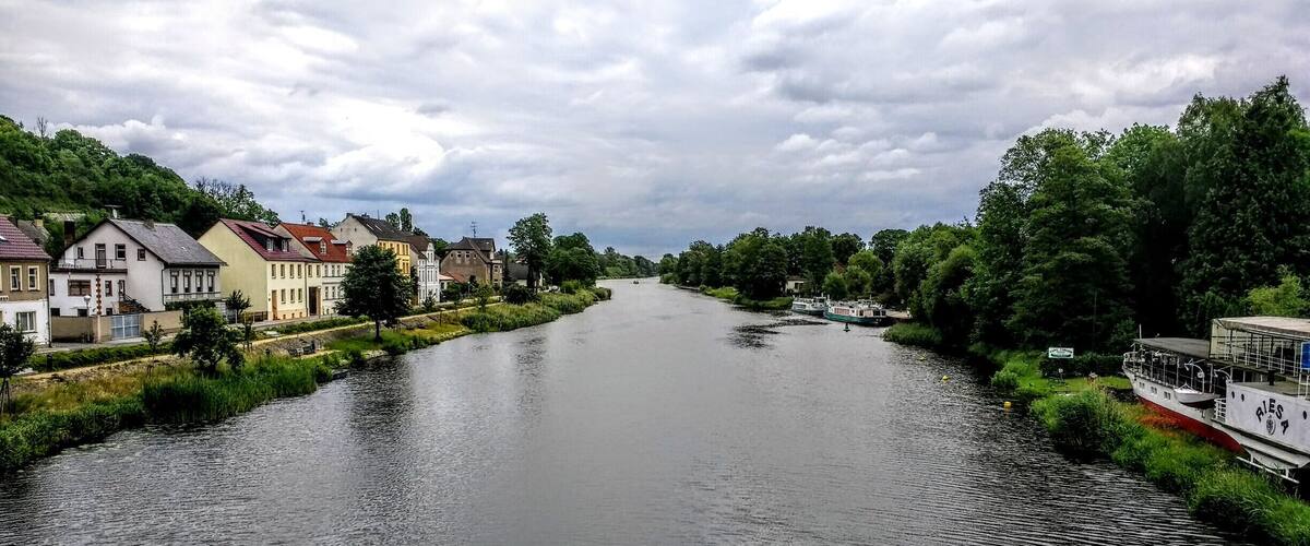 A river flanked by houses and greenery under a cloudy sky.