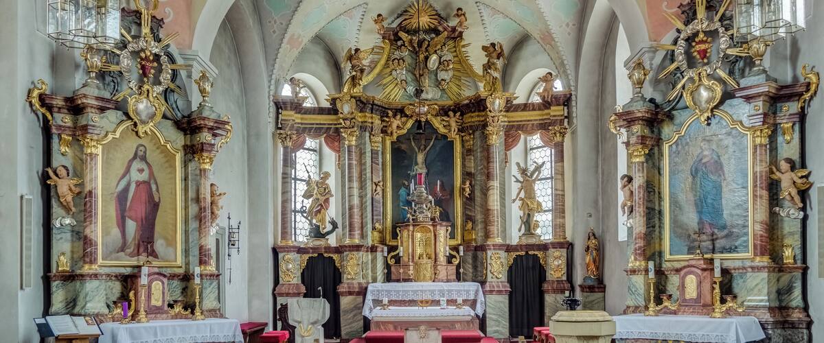 An ornate church interior with a central altar, religious paintings, and golden decorations.