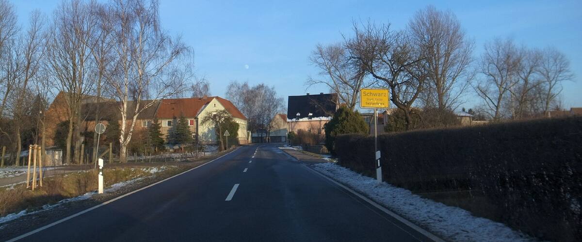 A rural road with houses on one side and a sign indicating 'Schwarz' and 'Stadt Calbe'.
