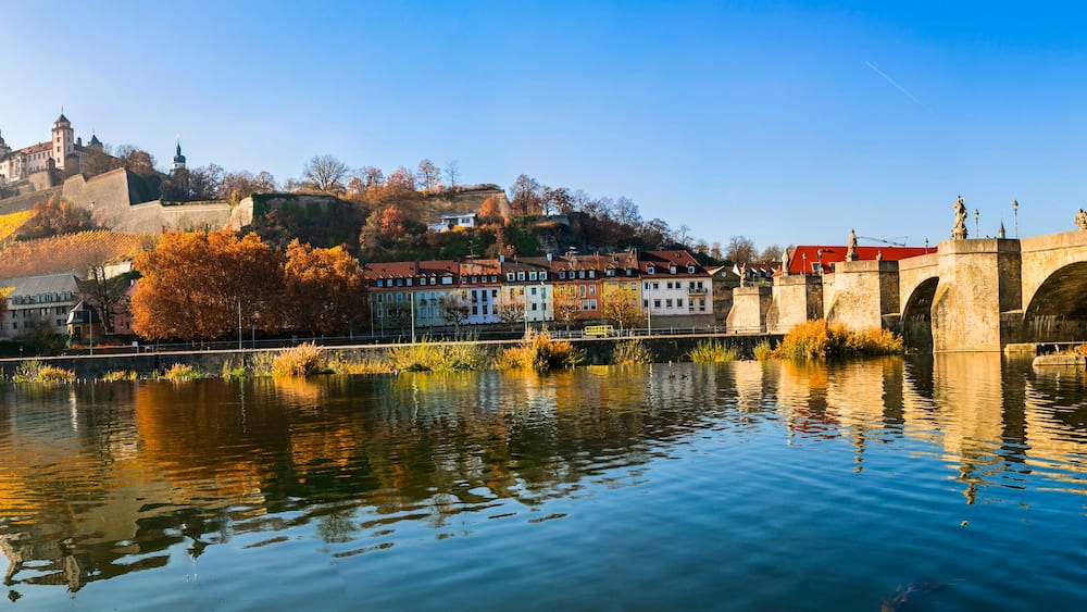 Une rivière traversée par un pont de pierre, des arbres aux couleurs automnales et un château perché sur une colline.