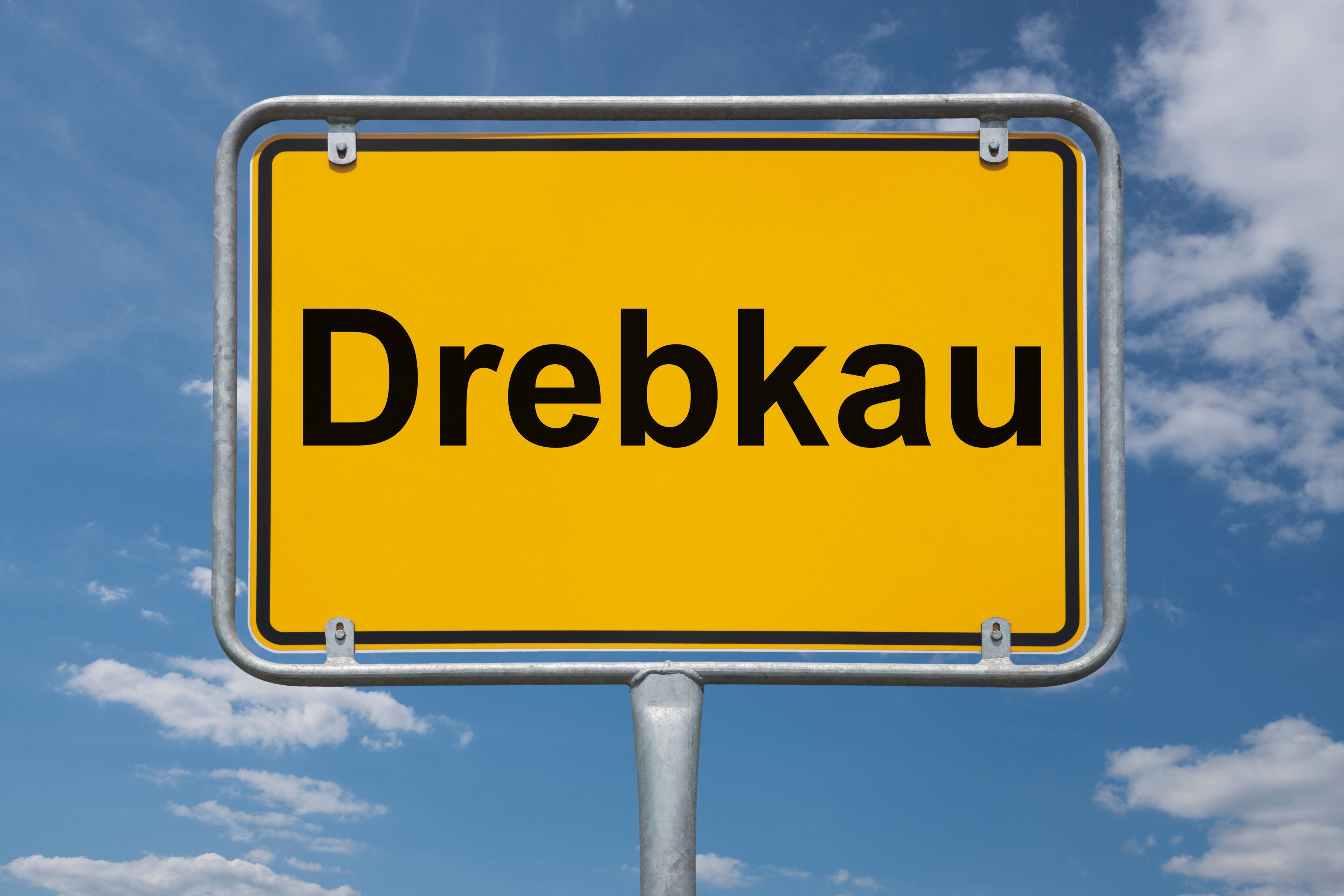 A yellow sign with the word "Dreibkau" against a blue sky with clouds.