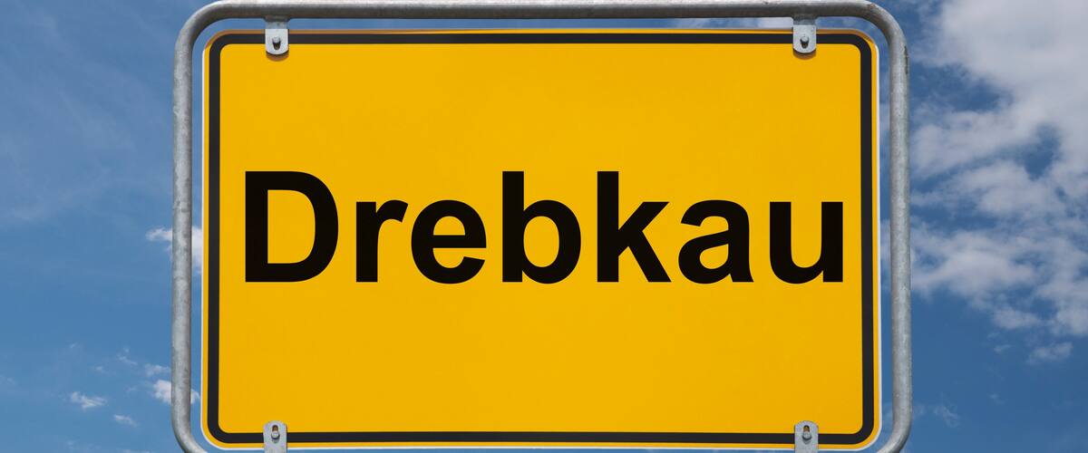 A yellow sign with the word "Dreibkau" against a blue sky with clouds.