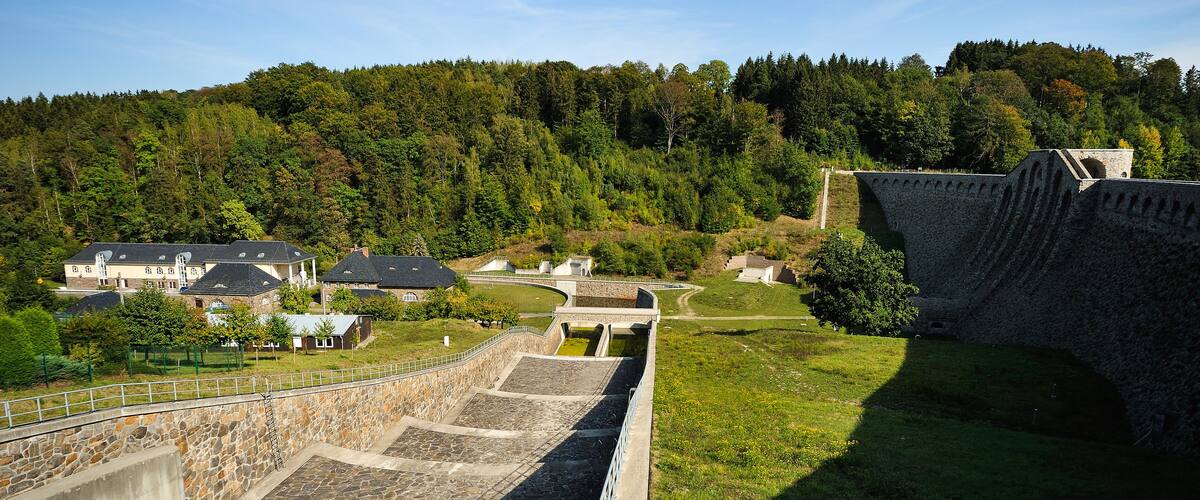 A stone dam with a water channel, surrounded by lush greenery and a forested hillside.