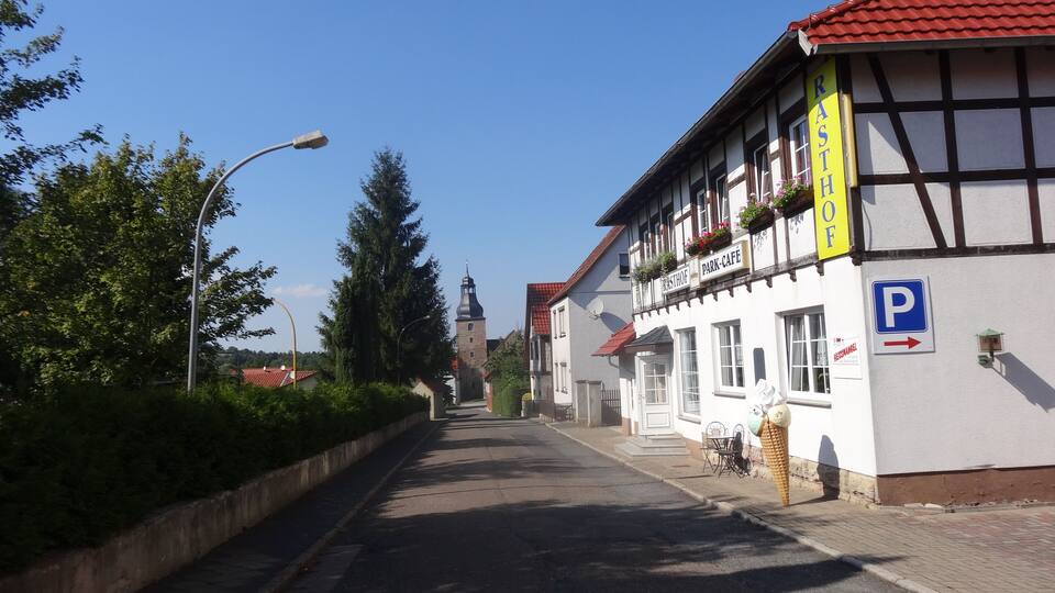 A street with a park cafe, a parking sign, and a traditional building with a red roof.