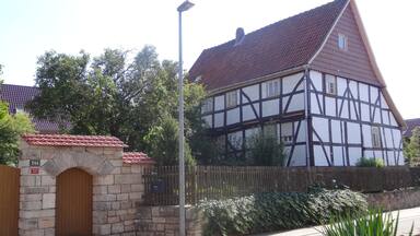 A traditional half-timbered house with a red-tiled roof, a stone archway, and a wooden fence.