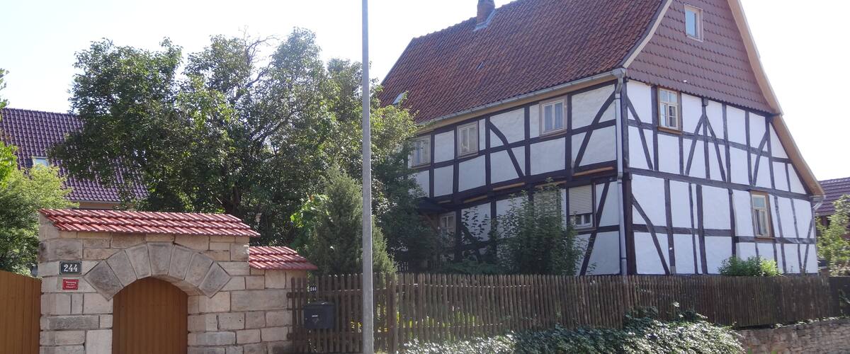 A traditional half-timbered house with a red-tiled roof, a stone archway, and a wooden fence.