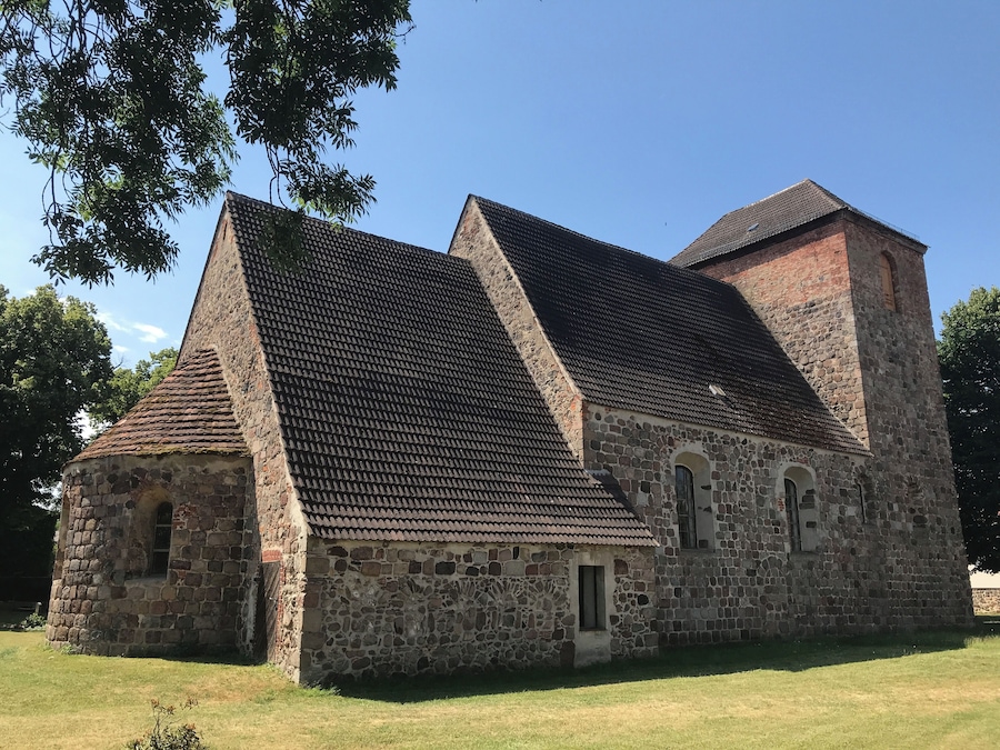 Een stenen kerk met een steil dak en een klokkentoren.