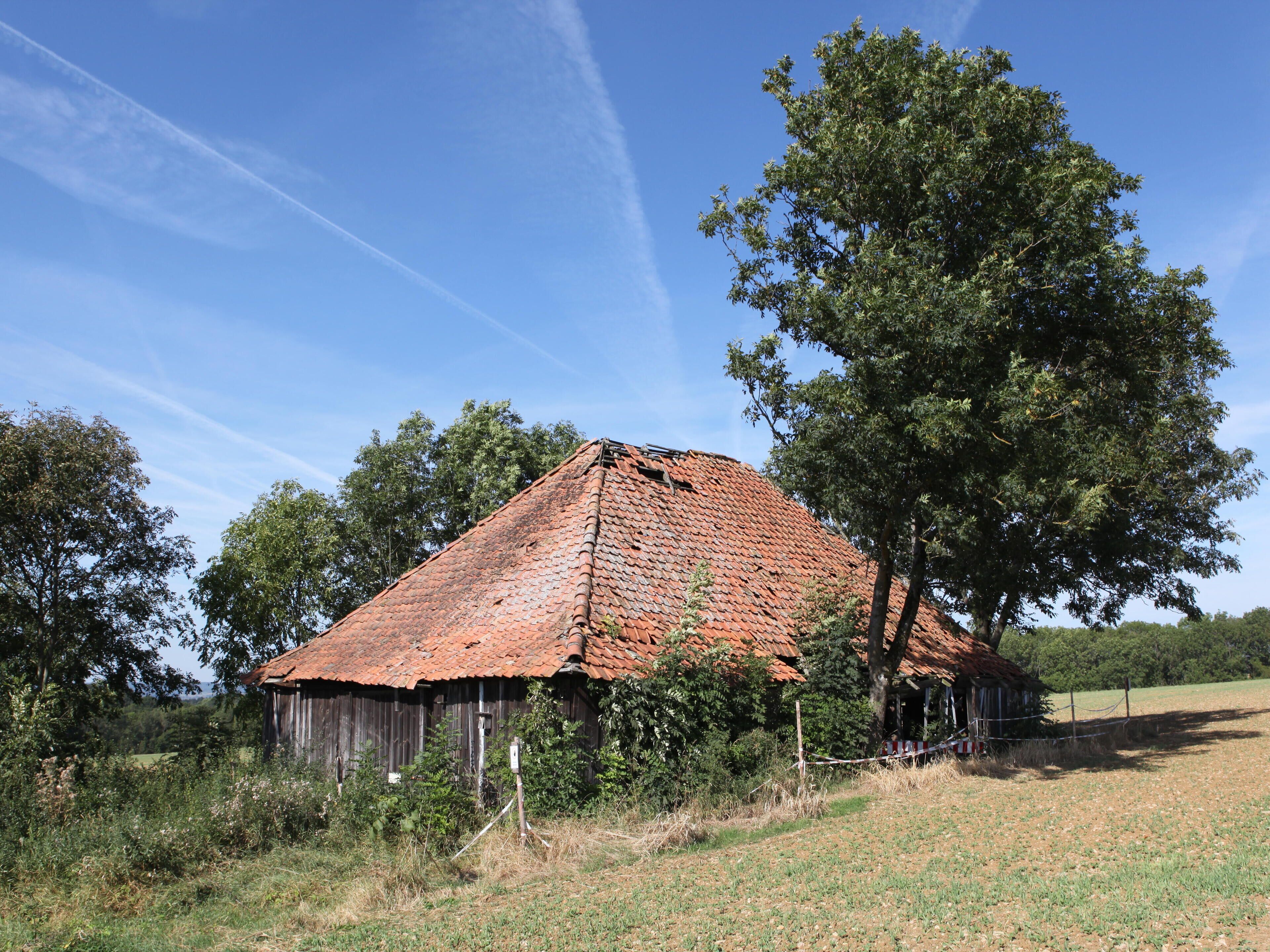 A rustic barn with a red-tiled roof, surrounded by trees and a grassy field.