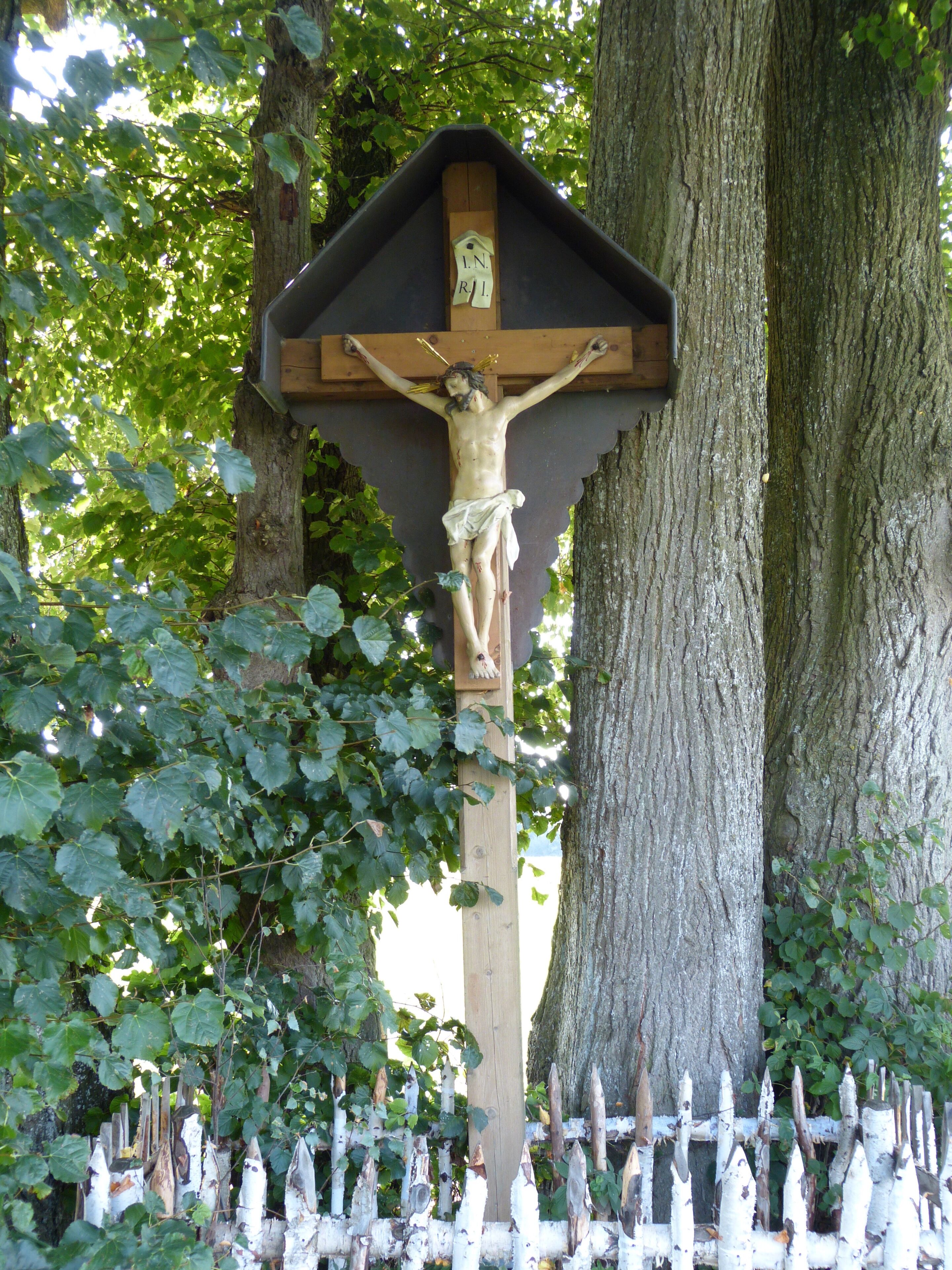 A wooden crucifix mounted on a tree, surrounded by a white picket fence.