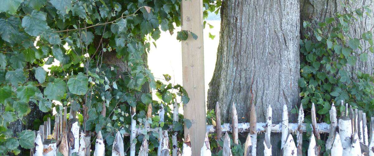 A wooden crucifix mounted on a tree, surrounded by a white picket fence.