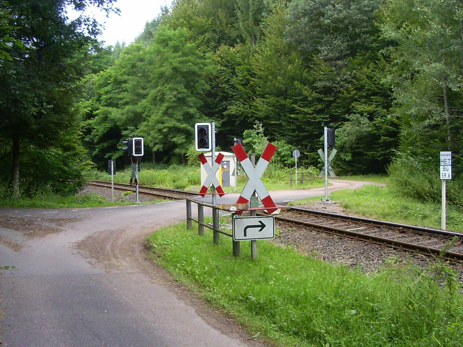 A railway crossing with barriers and warning lights, surrounded by greenery.