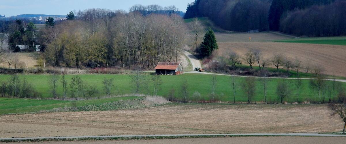 A rural landscape with a dirt road, a small red-roofed barn, and a tractor.