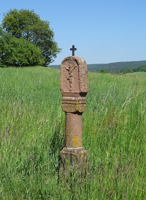 A weathered gravestone in a grassy field with a cross at the top and the year 1816 inscribed on it.