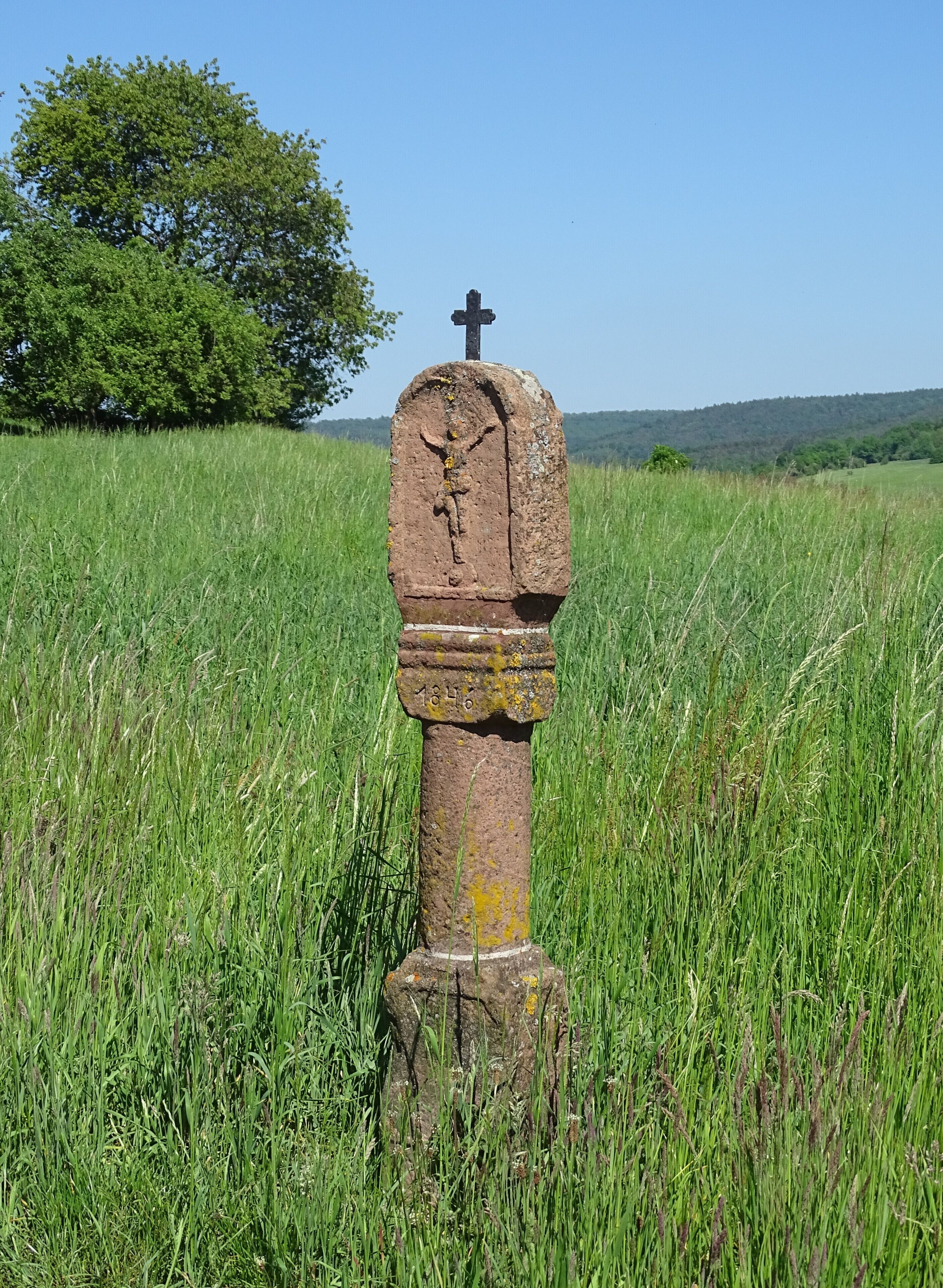 A weathered gravestone in a grassy field with a cross at the top and the year 1816 inscribed on it.