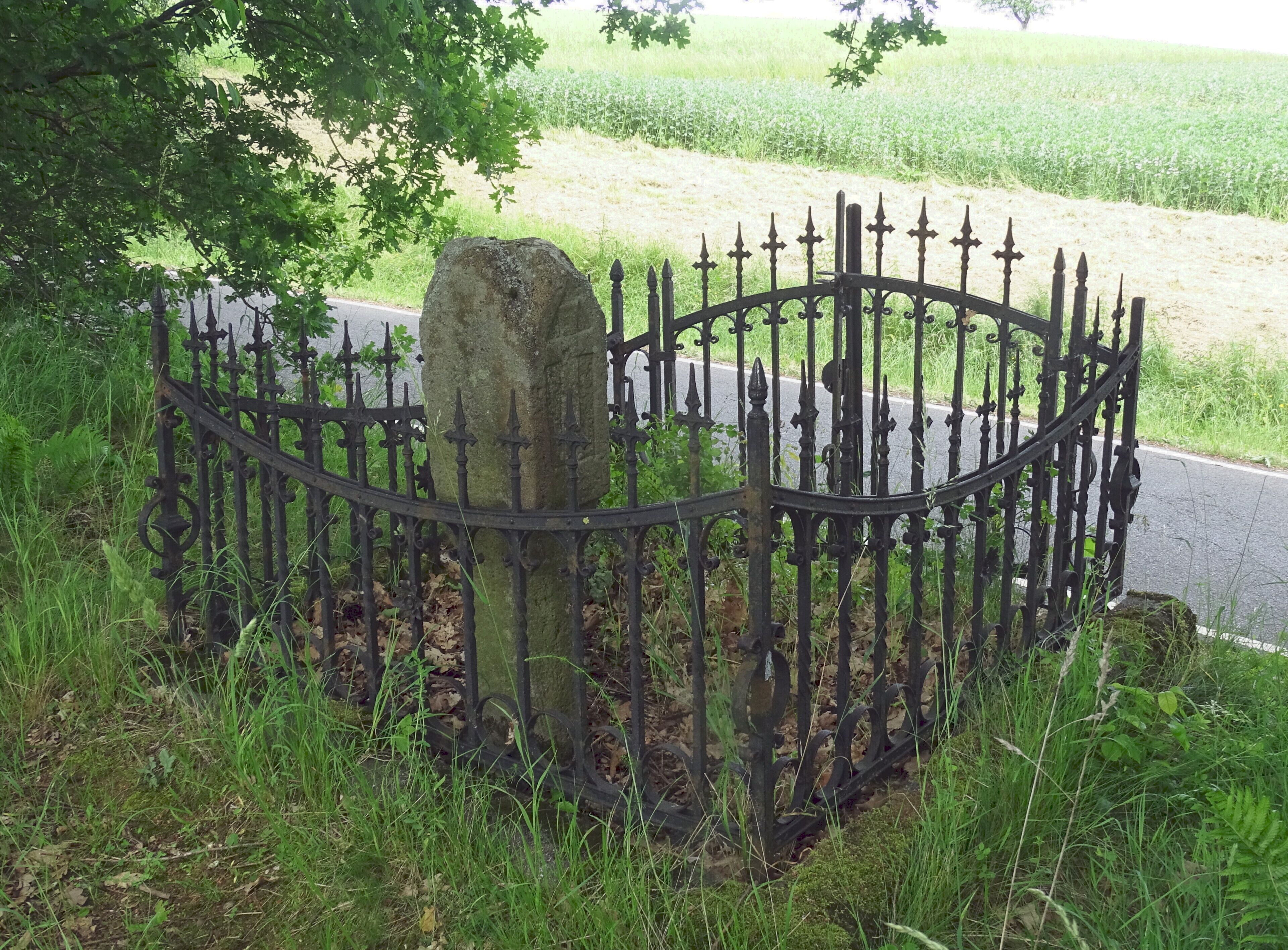 A stone headstone surrounded by a wrought iron fence in a grassy area.
