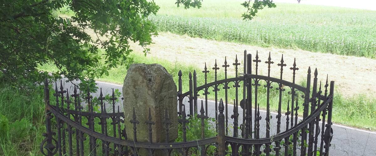 A stone headstone surrounded by a wrought iron fence in a grassy area.