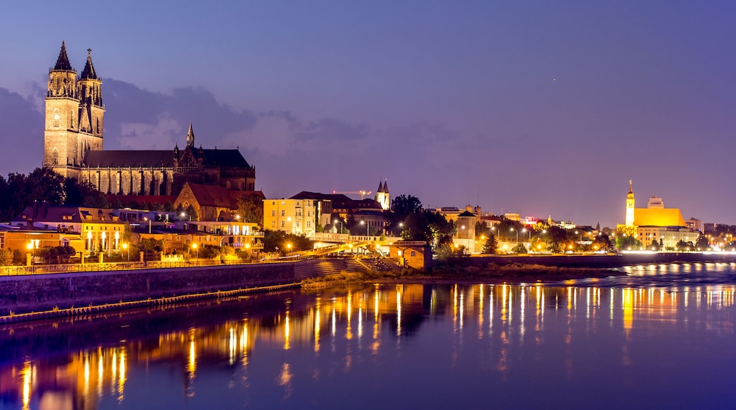 A historic cityscape with a prominent cathedral and tower, a river reflecting the lights, and a bridge connecting the two sides.