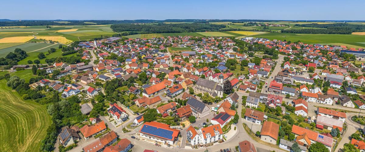 An aerial view of a rural village with red-roofed houses, green fields, and solar panels on buildings.