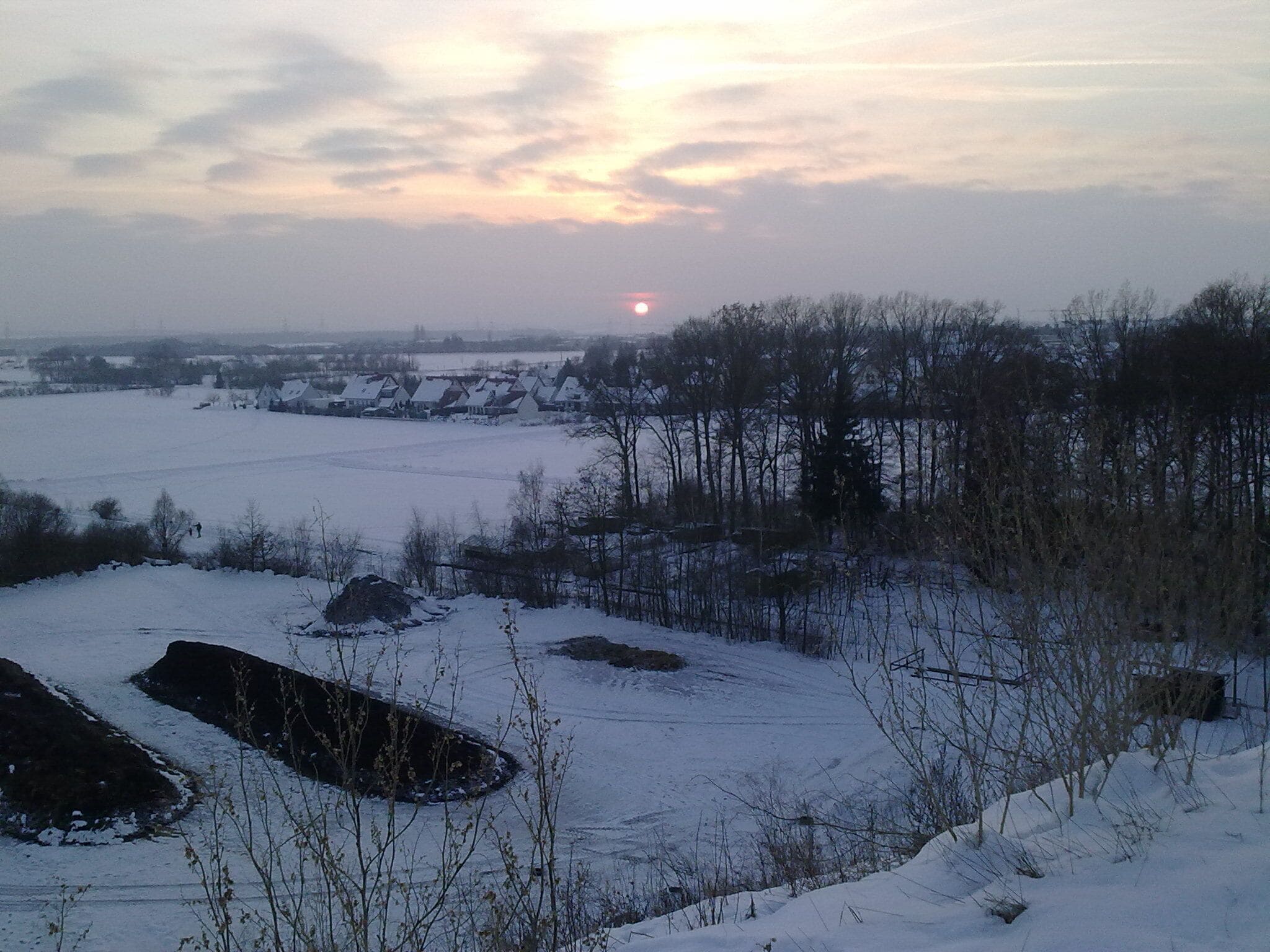 A snowy landscape with a sunset, a field, and a row of houses.