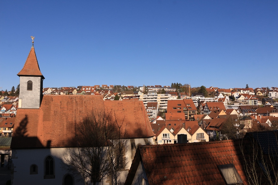 A town with a prominent church tower, red-roofed buildings, and a clear blue sky.