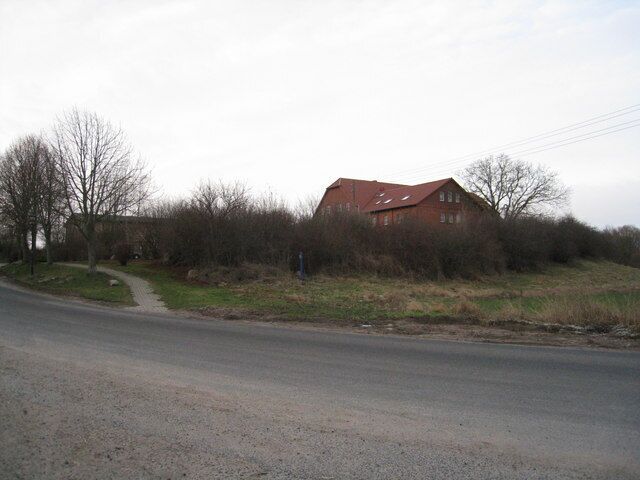 A rural road with a red-roofed building on the right, surrounded by trees and bushes.
