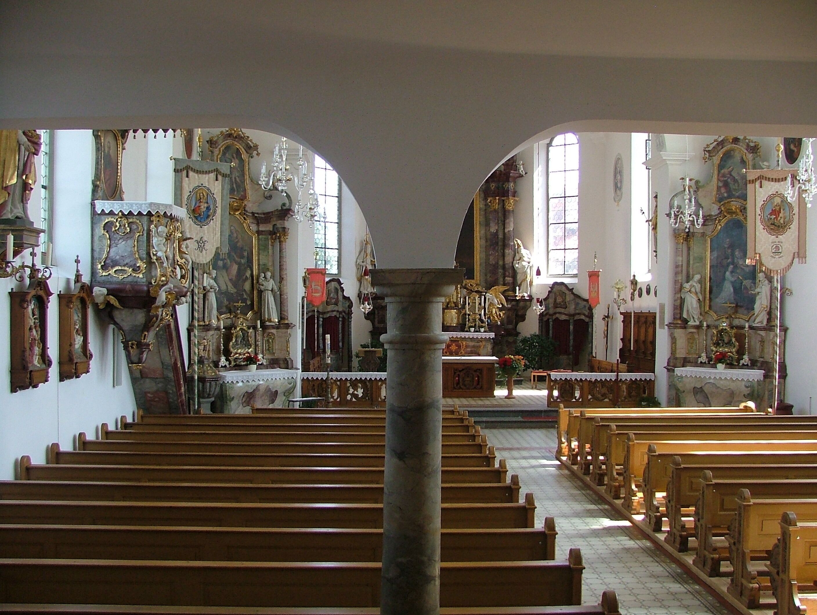 An ornate church interior with wooden pews, religious statues, and stained glass windows.
