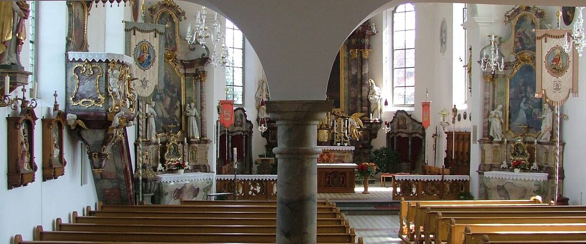 An ornate church interior with wooden pews, religious statues, and stained glass windows.