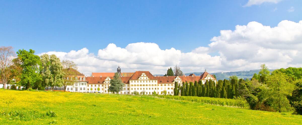 A large building complex with red roofs, surrounded by green fields and trees.