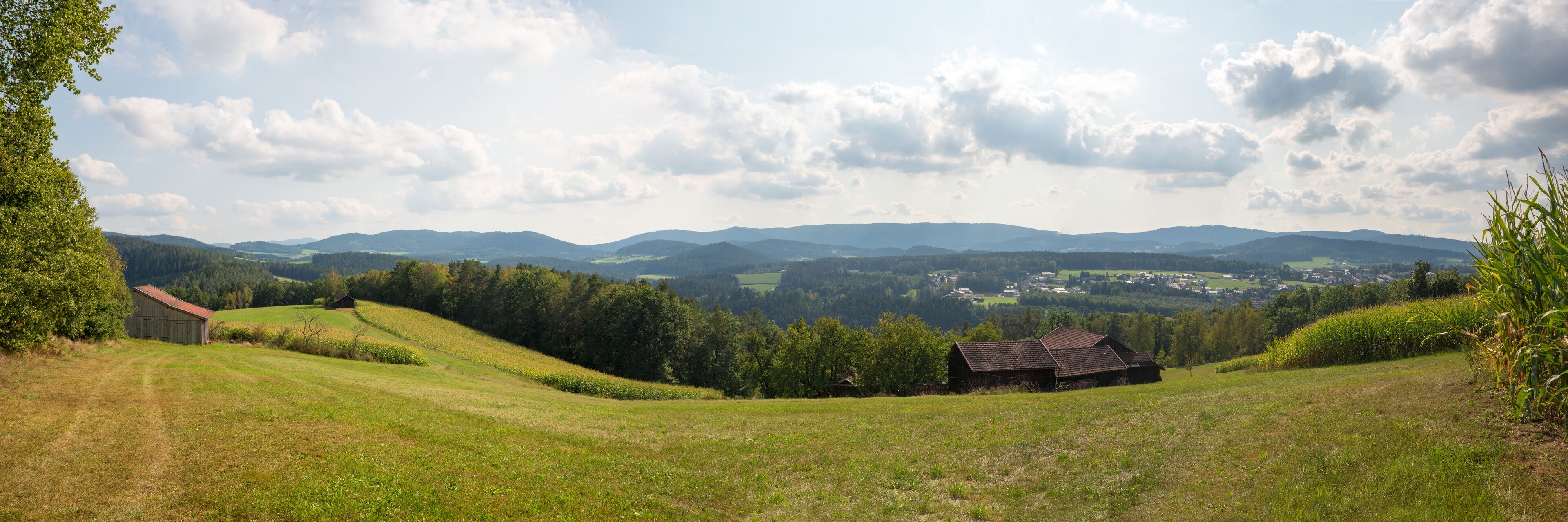 Rolling hills, a small wooden barn, and distant mountains under a partly cloudy sky.