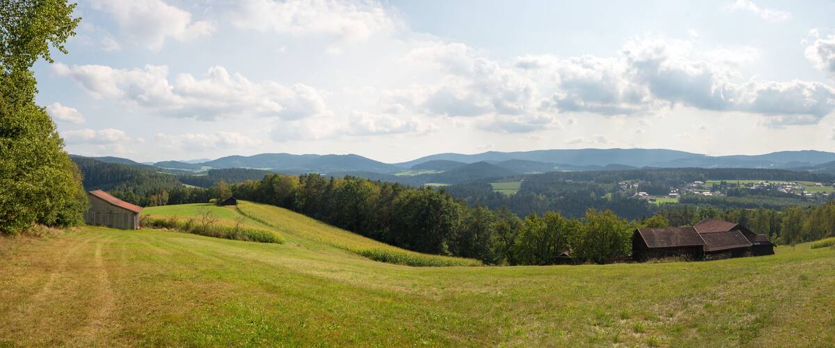 Rolling hills, a small wooden barn, and distant mountains under a partly cloudy sky.