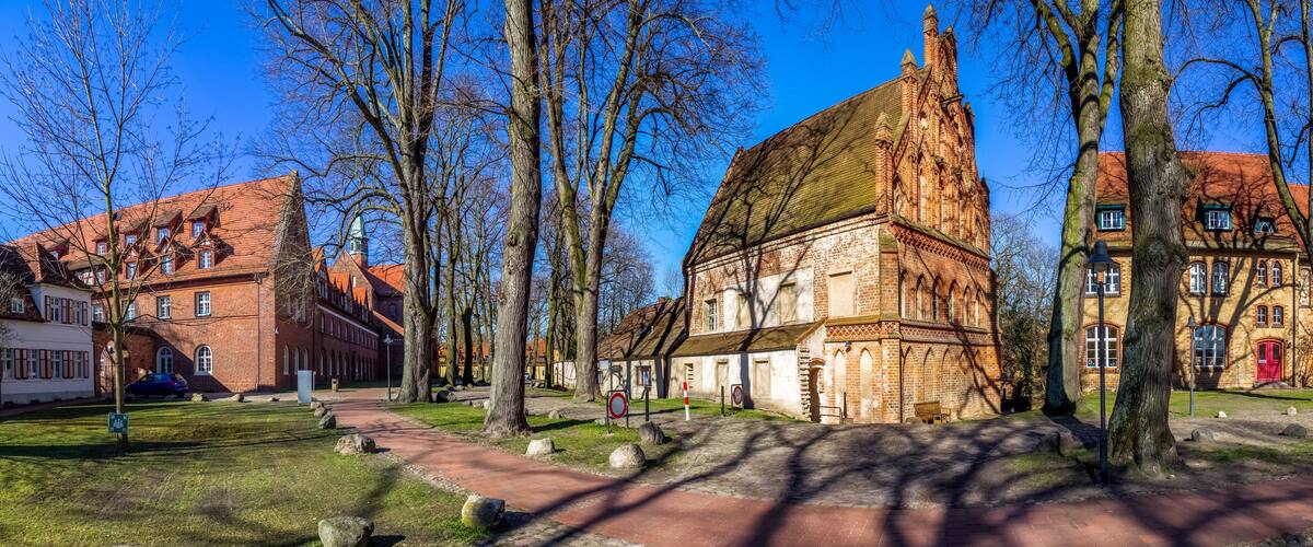 A historic building with a steep roof, surrounded by trees and a cobblestone path.