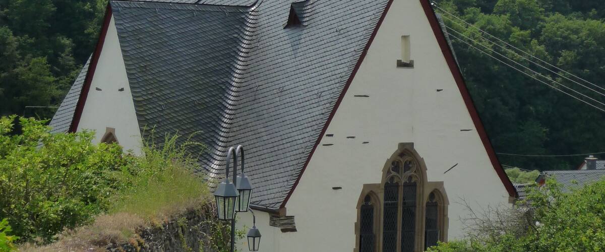 A church with a pointed roof and a weather vane on top, surrounded by lush greenery.