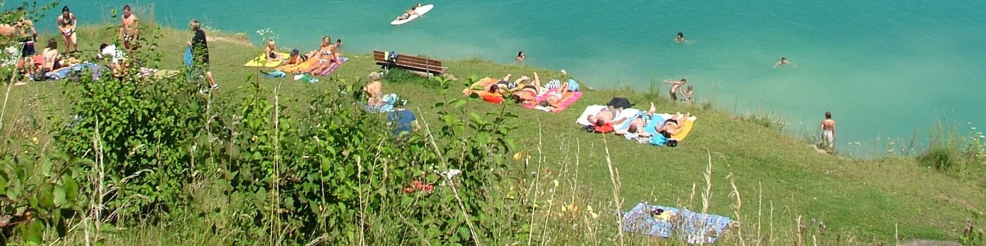 A lake with people swimming and sunbathing on the shore.