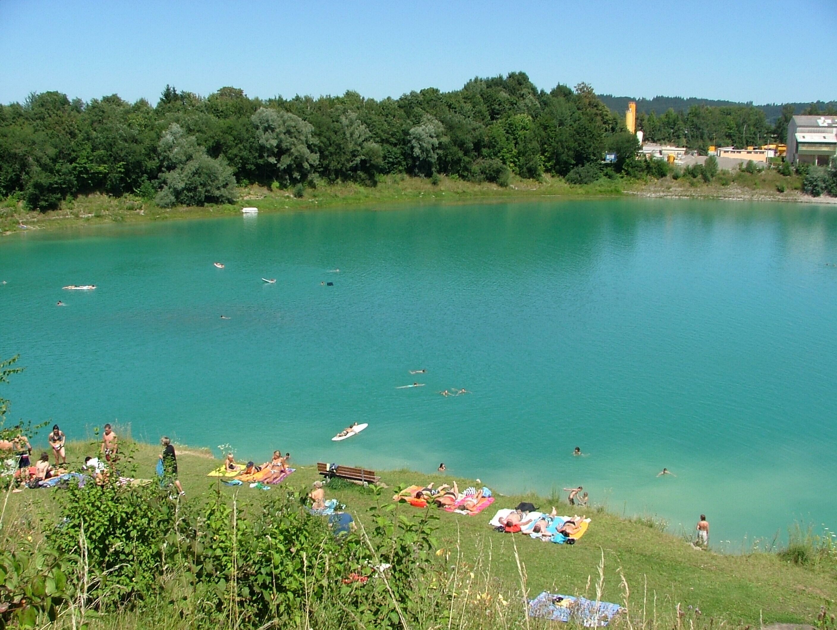 A lake with people swimming and sunbathing on the shore.
