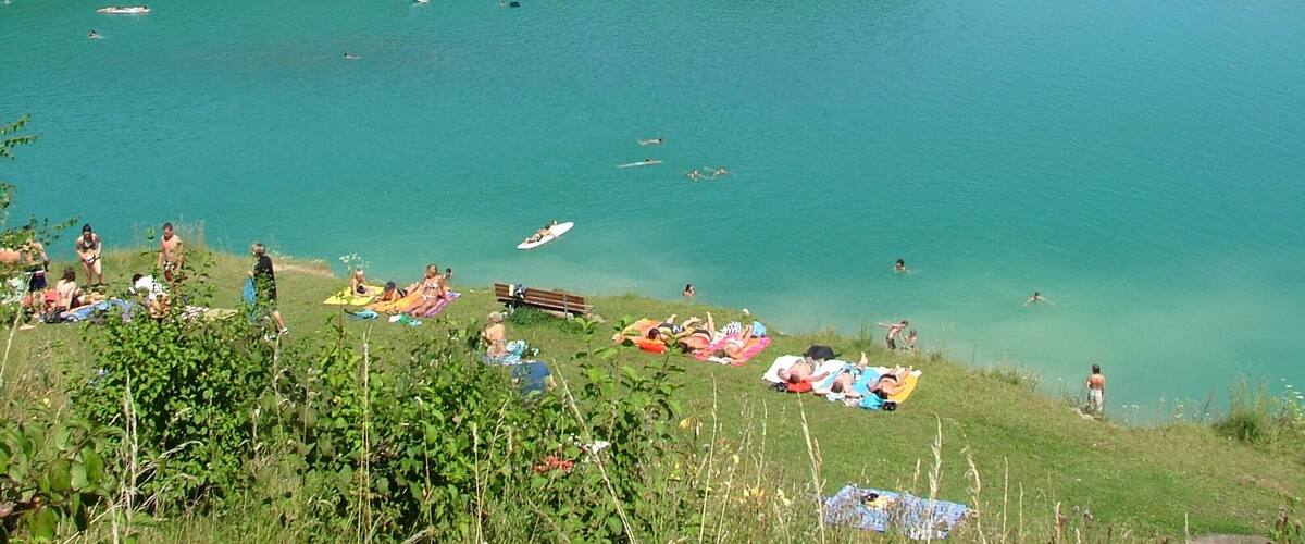 A lake with people swimming and sunbathing on the shore.
