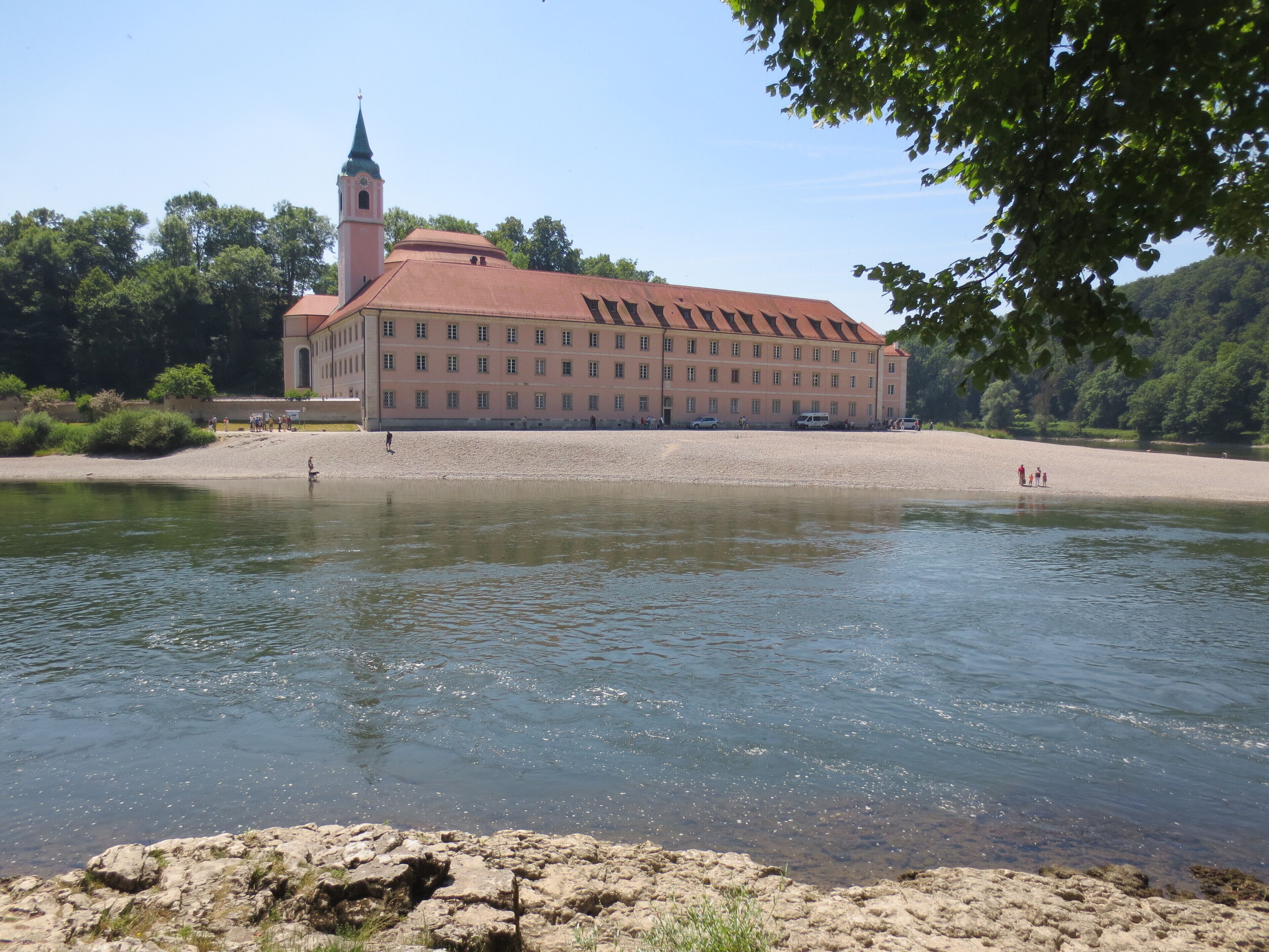 A large building with a red roof and a tower, situated by a calm river.