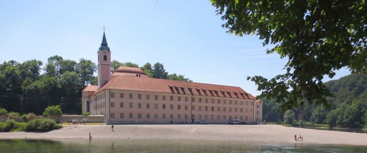 A large building with a red roof and a tower, situated by a calm river.