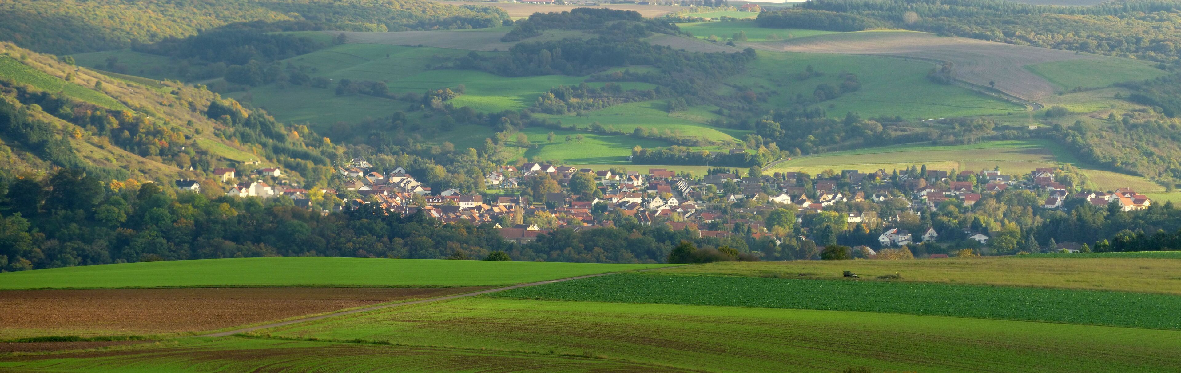 A rural landscape with rolling hills, a village with traditional houses, and expansive green fields.
