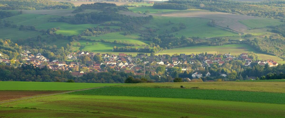 A rural landscape with rolling hills, a village with traditional houses, and expansive green fields.