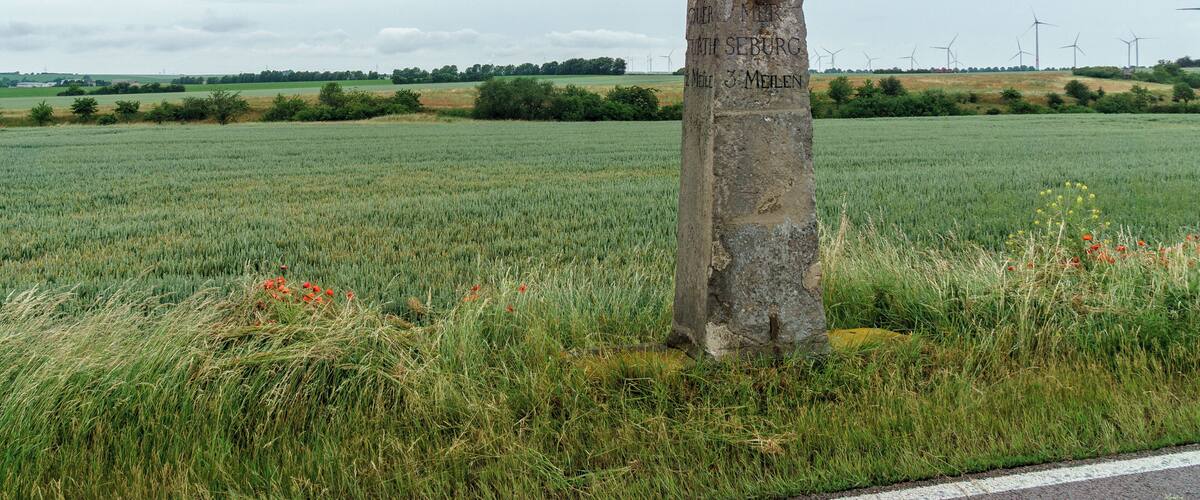 A stone monument in a field with wind turbines in the background.