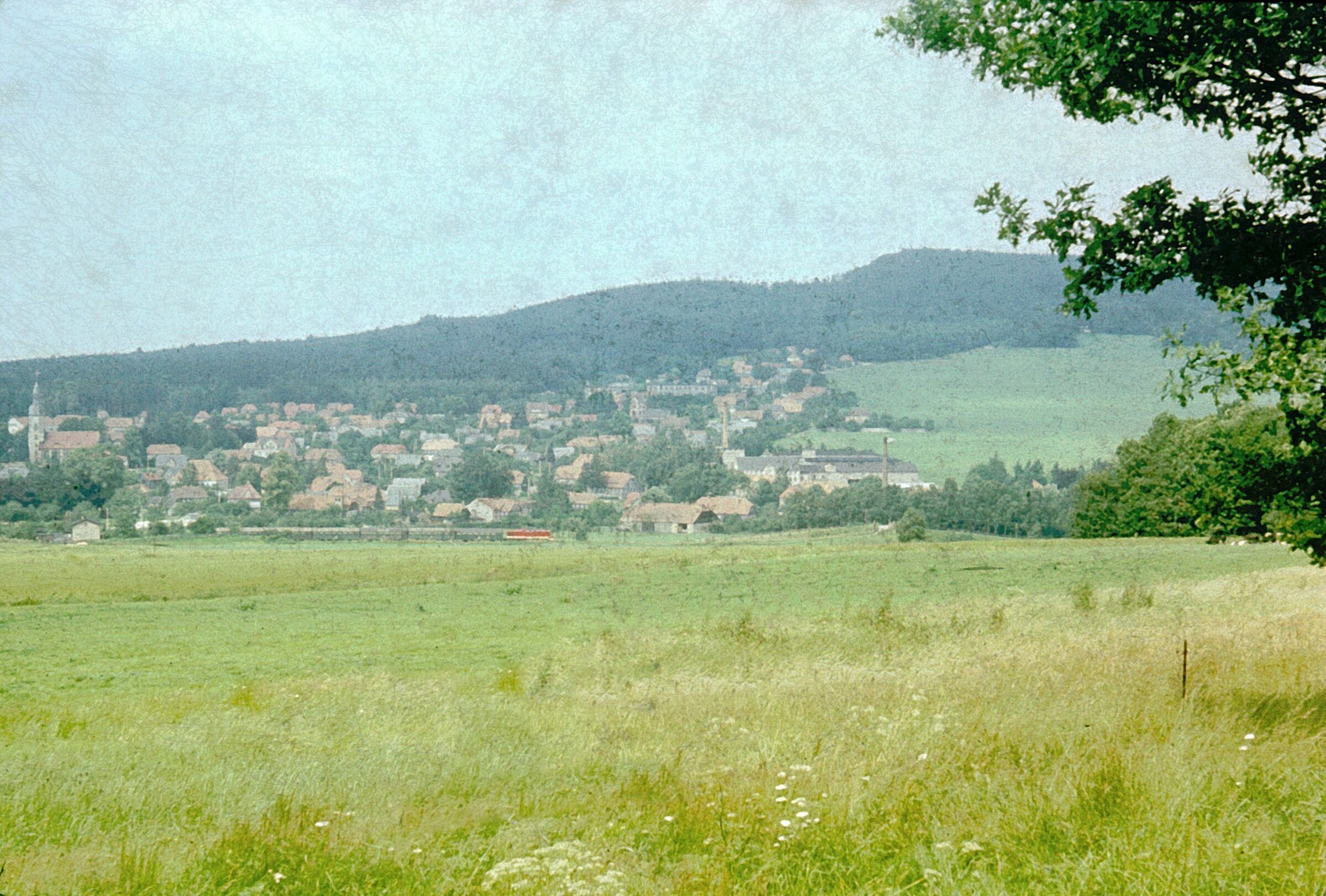 A rural landscape with a village nestled in the valley, surrounded by hills and greenery.