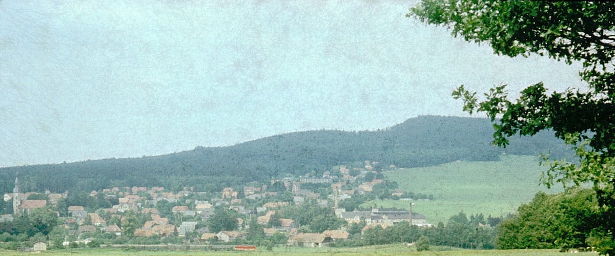 A rural landscape with a village nestled in the valley, surrounded by hills and greenery.