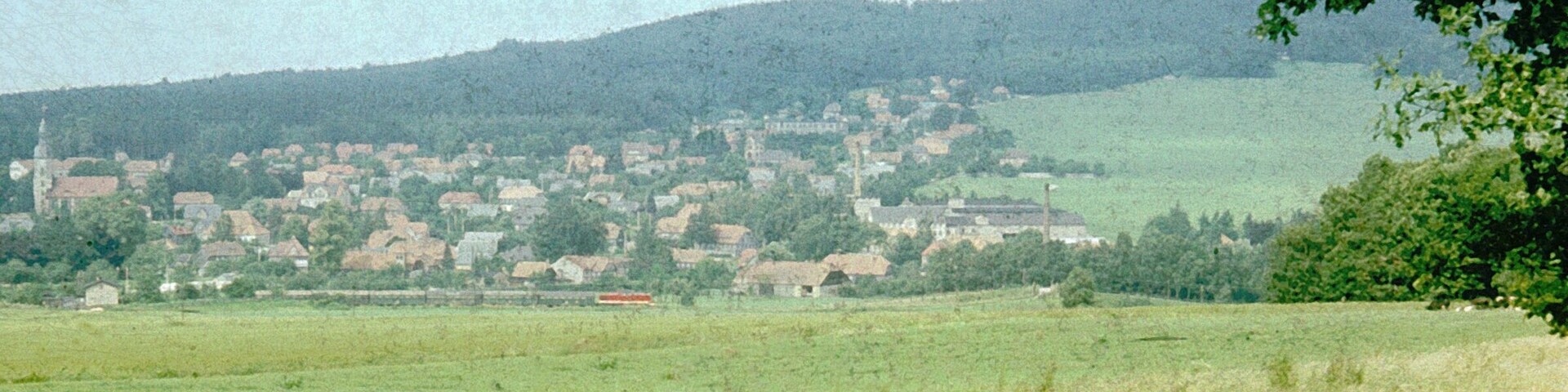 A rural landscape with a village nestled in the valley, surrounded by hills and greenery.