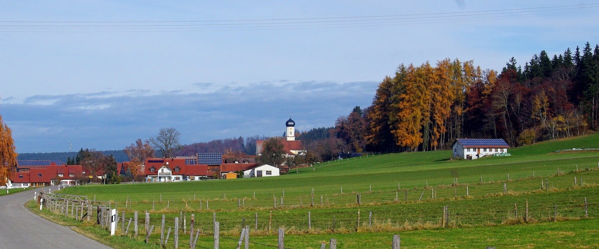 A rural landscape with a road, houses, a church, and autumn trees.
